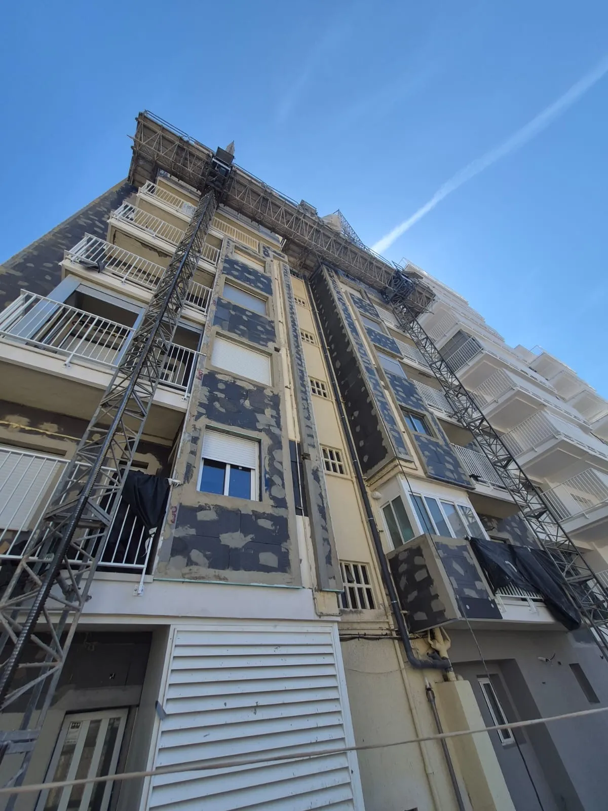 Fachada con placas de aislamiento térmico SATE y montacargas de obra